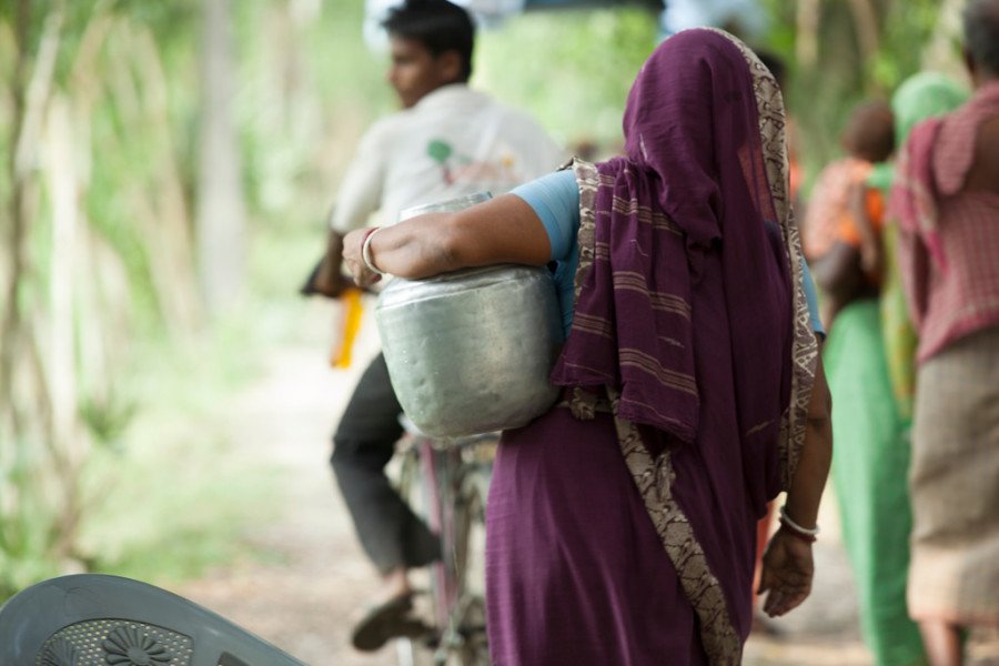 A woman in a colorful dress walking away carrying a silver jar