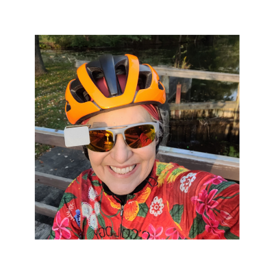 Sarah Hanly in a flowery bike jersey, orange helmet, and sunglasses