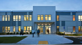 A picture of a beautiful brick school building with nice landscaping in front of it and a cloudy sky backdrop.