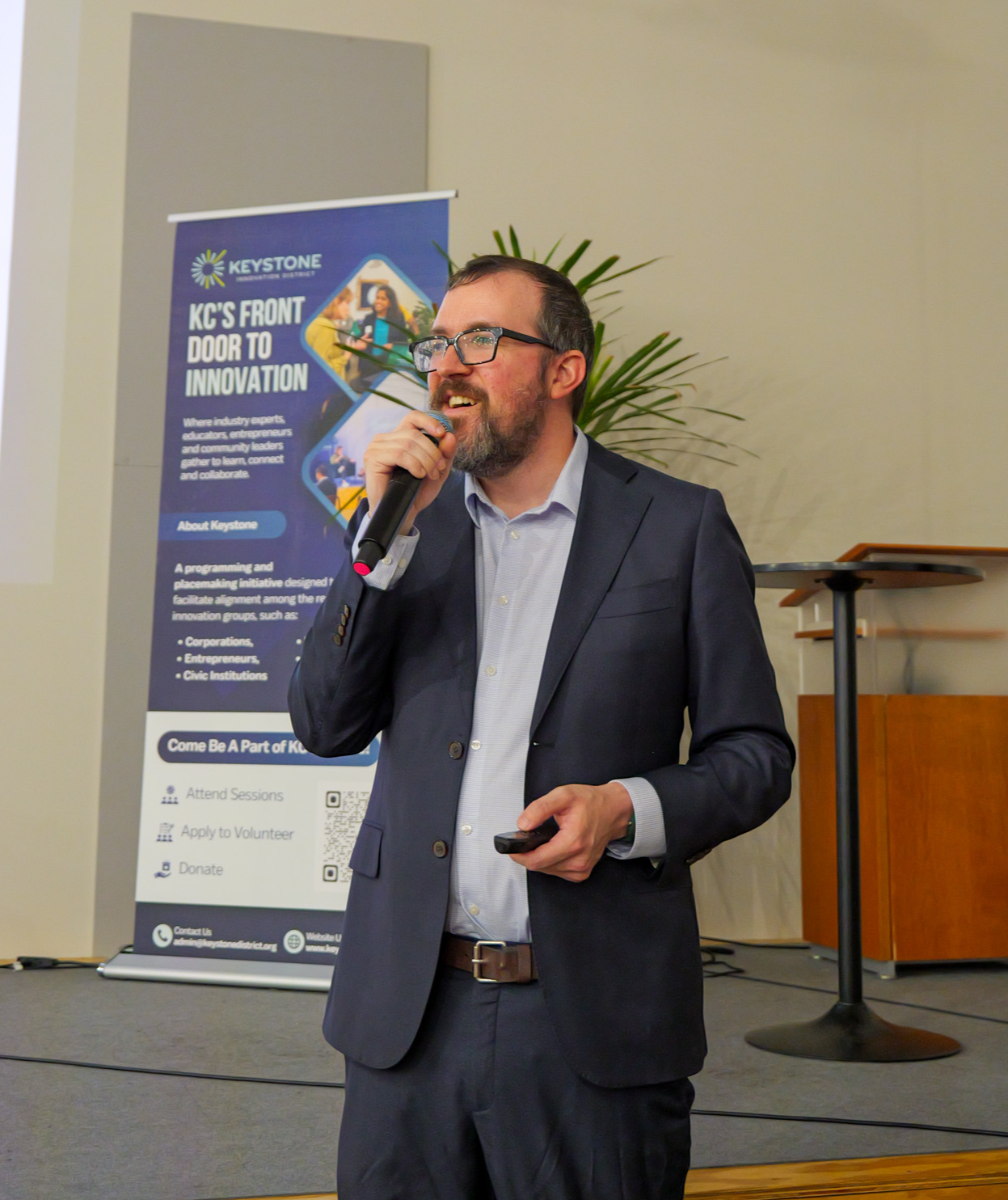 Trivia presenter, Travis Stull speaking during the 2026 trivia event in a dark grey suit