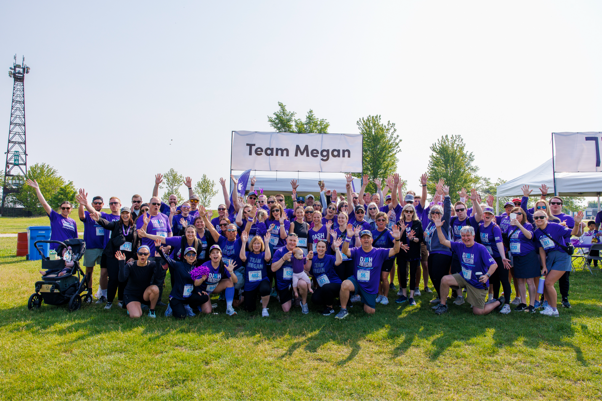large group of people smiling with their hands in the air infront of a Team Megan banner