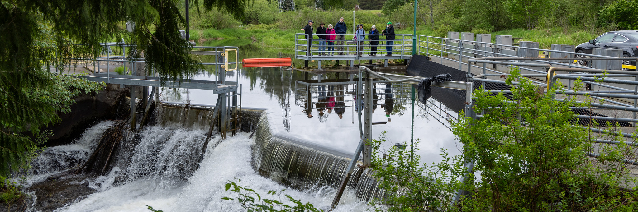 People gathering on a metal walkway watching rushing water