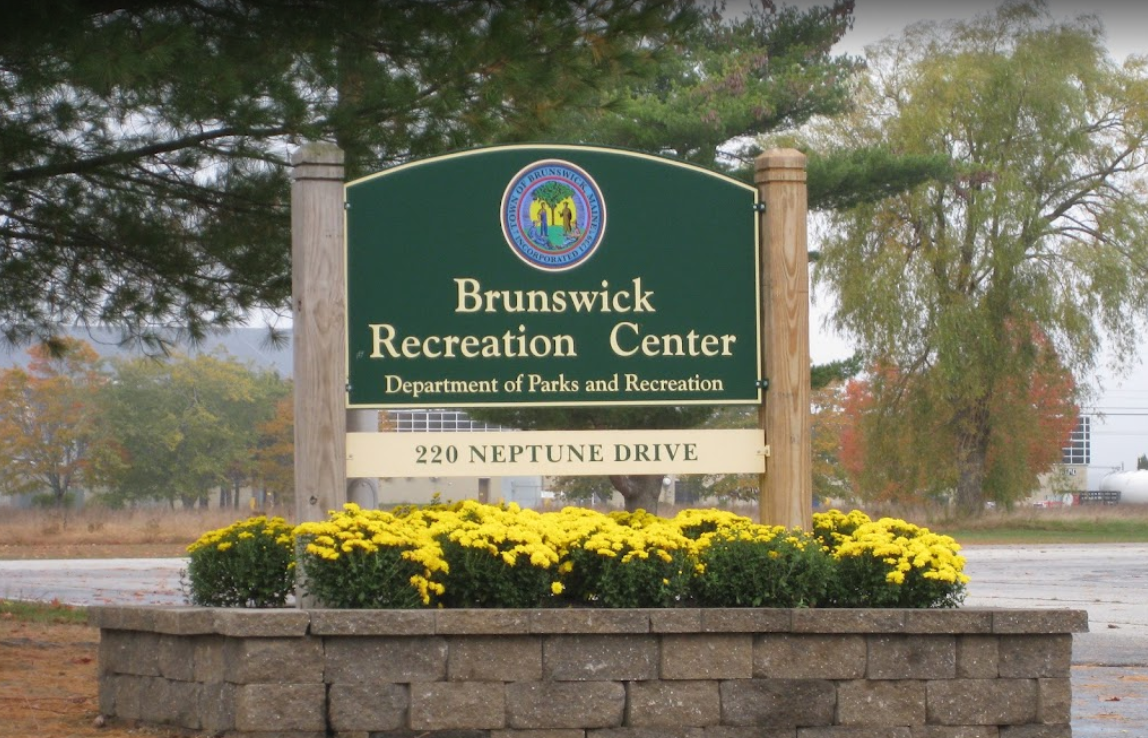 A picture of a beautiful brick school building with nice landscaping in front of it and a cloudy sky backdrop.