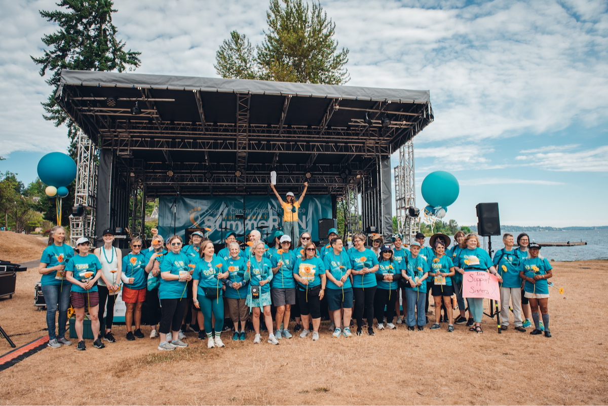 A large group of ovarian cancer survivors, all wearing teal, are honored on stage at SummeRun