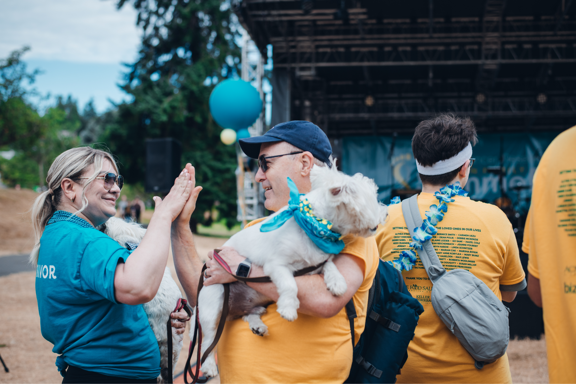 A small girl wearing a rainbow skirt stands in front of a wall that reads "We honor. We celebrate. We remember." The wall is covered in sticky notes with names.