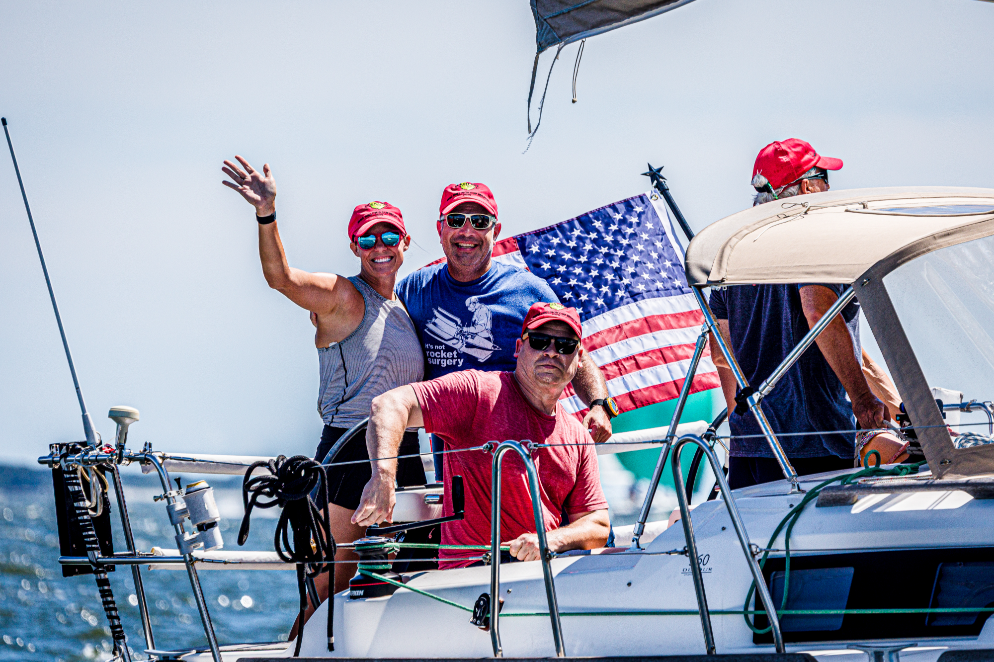 Four sailors wave and hug aboard a sailboat