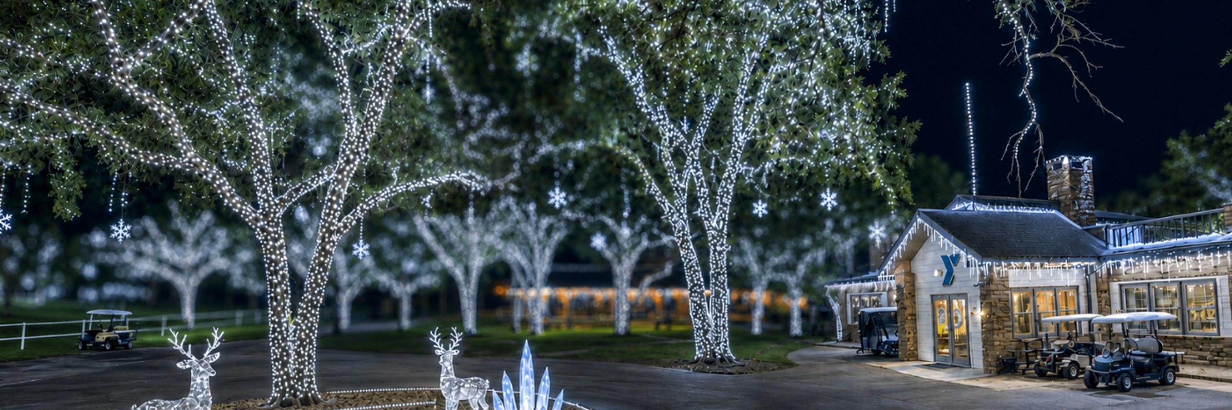 Trees wrapped in white lights, lit reindeer, and the lodge at YMCA Camp Carter at night