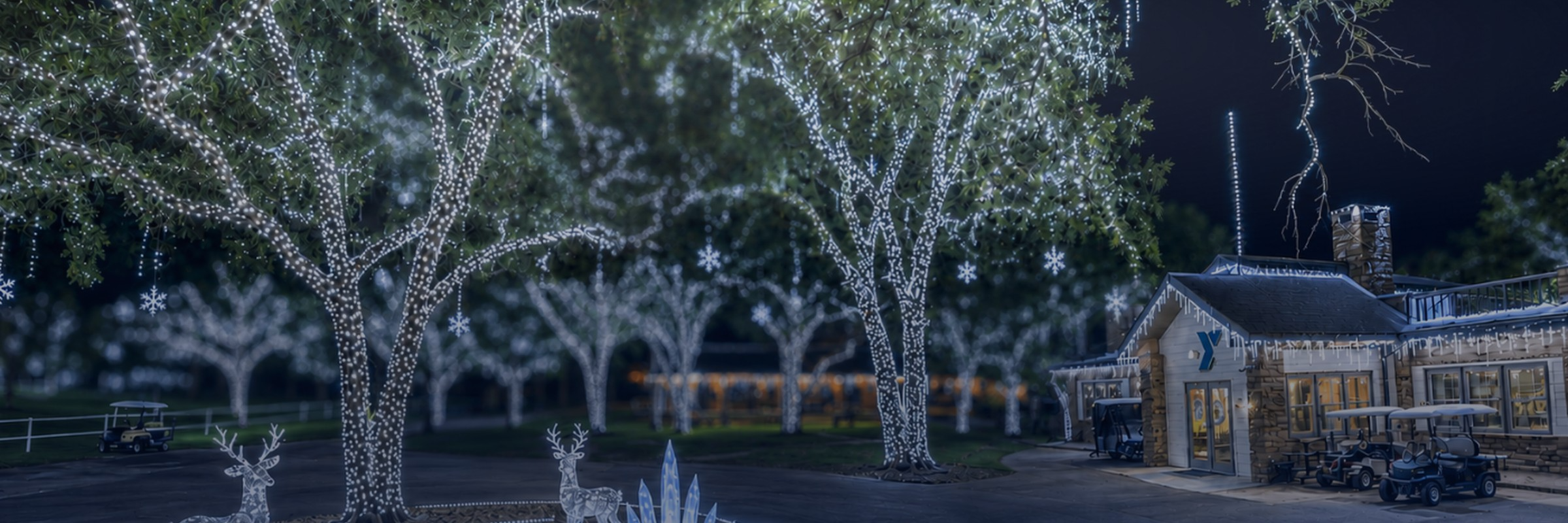 Trees wrapped in white lights, lit reindeer, and the lodge at YMCA Camp Carter at night