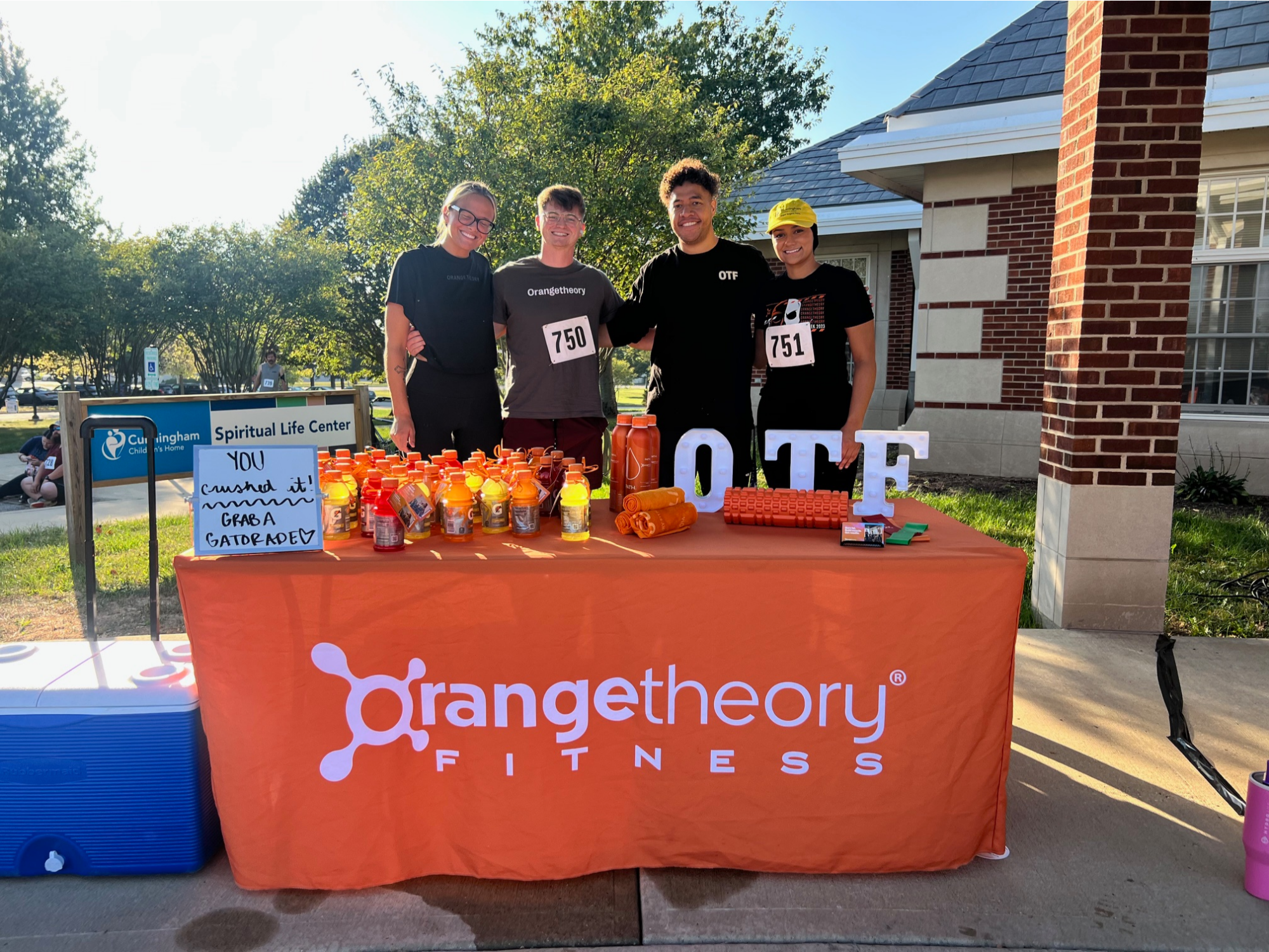 four staff members standing behind a table with an orange tablecloth and giveaways on top