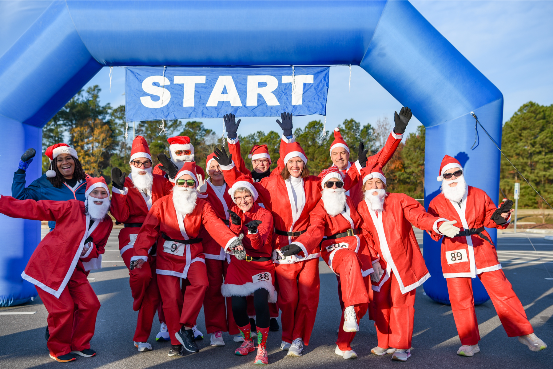 Runners in Santa Suits at the starting line smiling at the camera excited to run or walk!