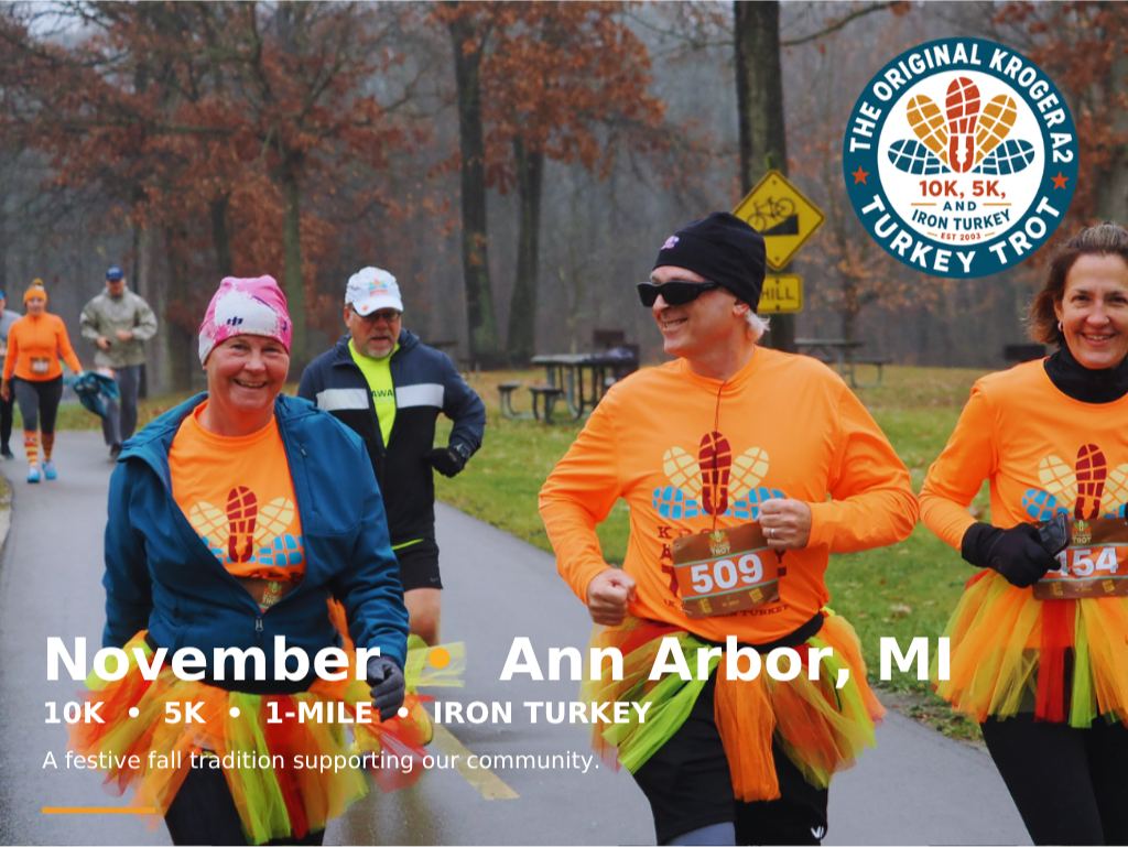 Smiling participants wearing orange and brown shirts with tutus taking their time to enjoy the annual Ann Arbor Turkey Trot 1 Mile, 5K, and 10K walk/run at Hudson Mills Metropark in Dexter, Michigan