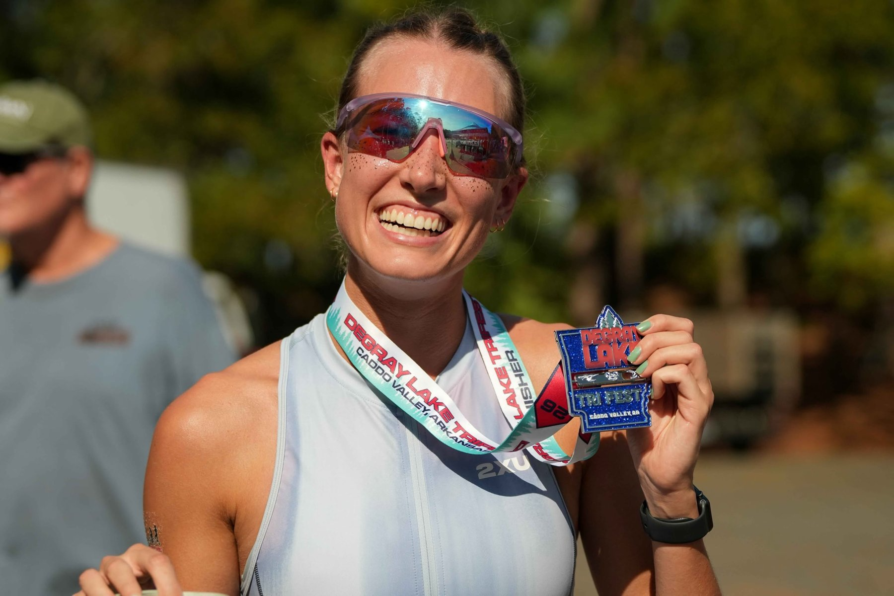 Finisher smiling and holding up her DeGray Lake Triathlon finisher medal